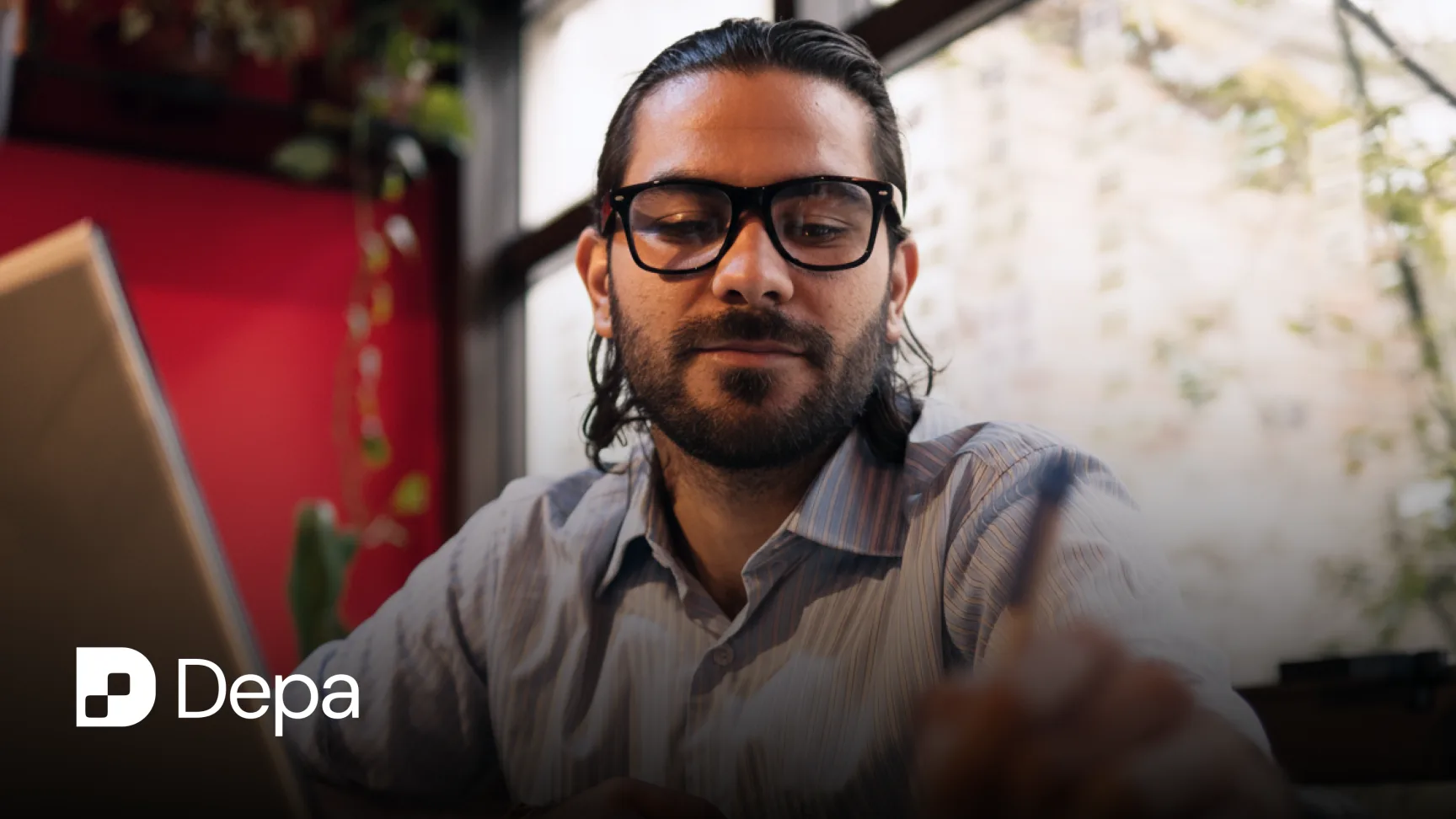A man in glasses works at a laptop in a warmly lit interior, with the Depa logo