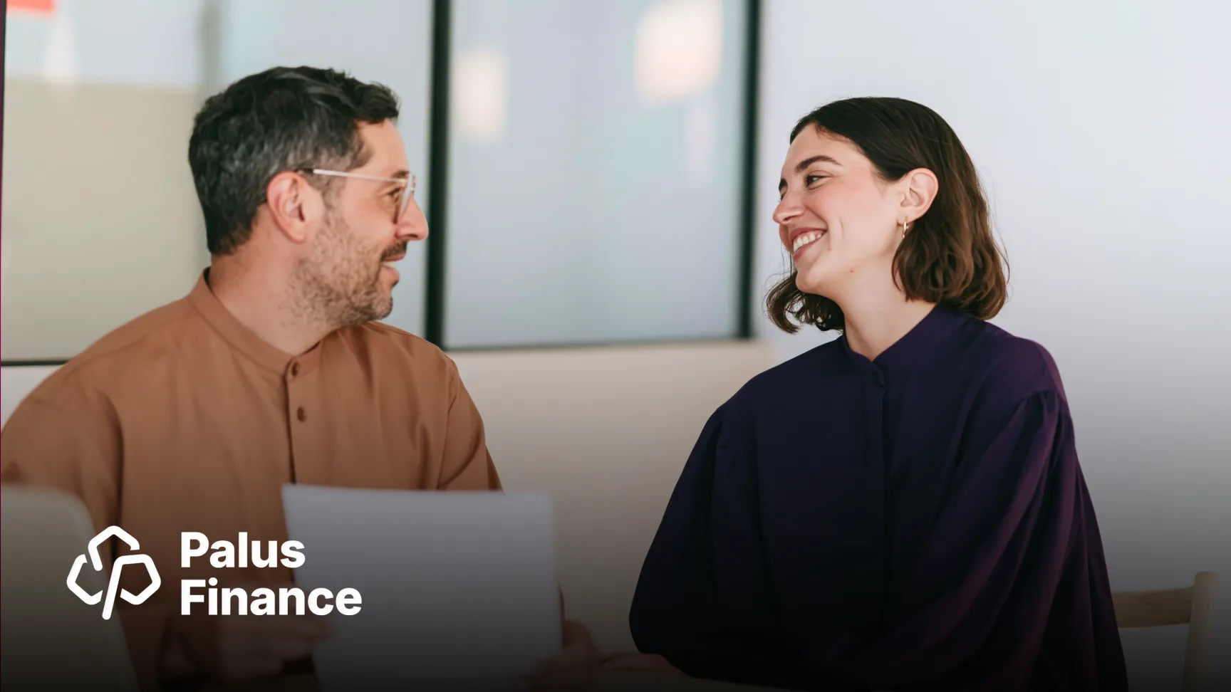 Two colleagues laugh together over a laptop in an office, with the Palus Finance logo